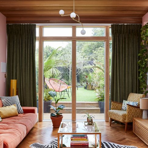A 70s style living room with large glass doors dressed in deep green curtains 