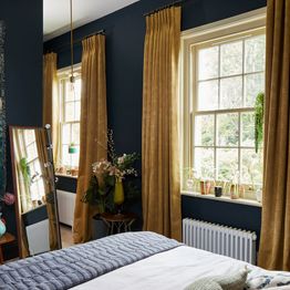A dark blue bedroom with two windows dressed in gold coloured curtains