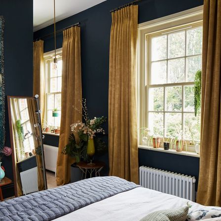 A dark blue bedroom with two windows dressed in gold coloured curtains