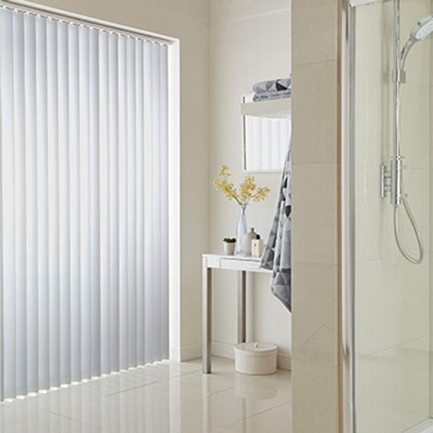 White coloured vertical blinds fitted to a wide window in a bathroom that is decorated in white