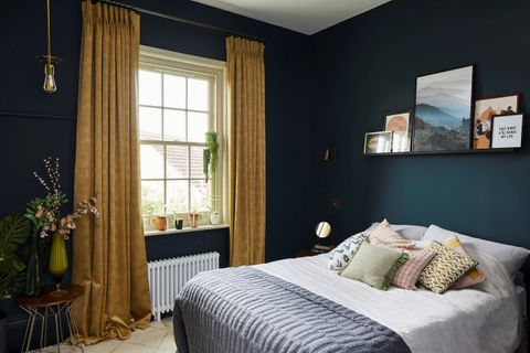 A navy blue bedroom with a window dressed with gold curtains