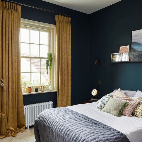 A navy blue bedroom with a window dressed with gold curtains