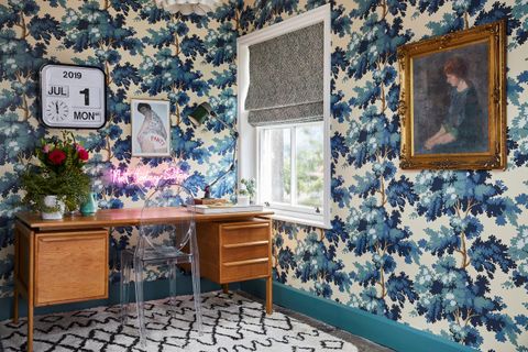 An office space with blue and white patterned wallpaper and a vintage writing desk