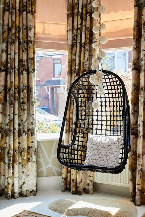 Hanging chair  in front of bay window dressed with floral velvet curtains 