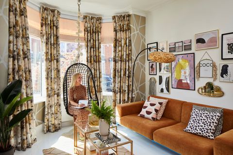 A woman sat in a 70s style living room with floral curtains