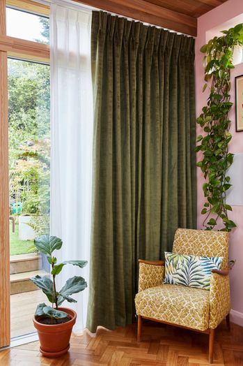 A floor to ceiling window with dark green curtains and a white Voile