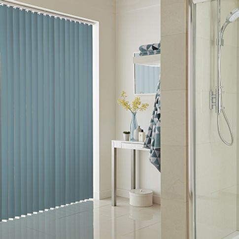 Light blue vertical blinds fitted to a wide window in a bathroom that is decorated in white