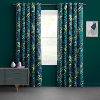 Blue and green coloured leaf patterned curtains with a black base colour fitted to a window in a tall window against a dark green wall