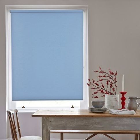 Blue roller blind fitted to a rectangular window in a dining room decorated in white and features a wooden dining table and chairs