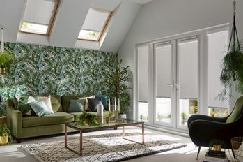four light grey perfect fit blinds partially open on door length windows in a grey room with green furnishings and plants including a feature wall of plant themed wallpaper