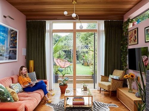 Dark floor to ceiling curtains are fitted to a wide door window along with voile curtains in a living room featuring a yellow armchair and blush sofa
