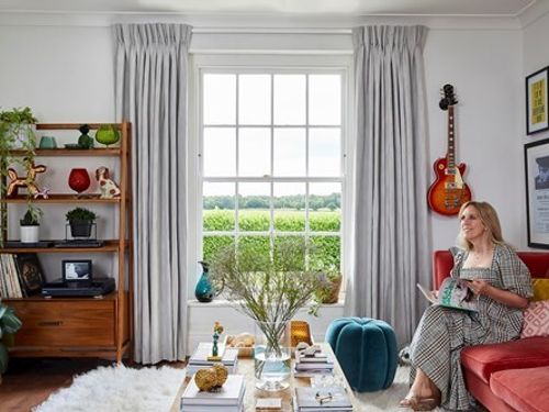 Interior designer Lisa Dawson sat in a white decorated living room with white curtains fitted to a tall rectangular window