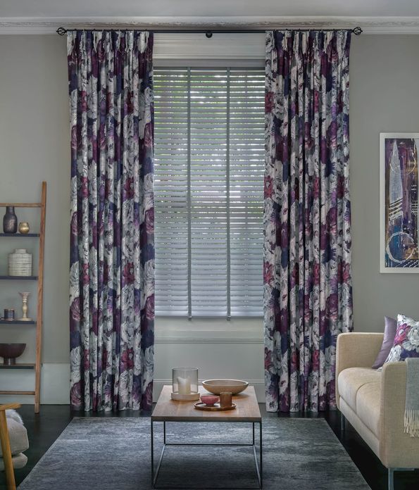 Living room with purple floral curtains layered over faux wood blinds