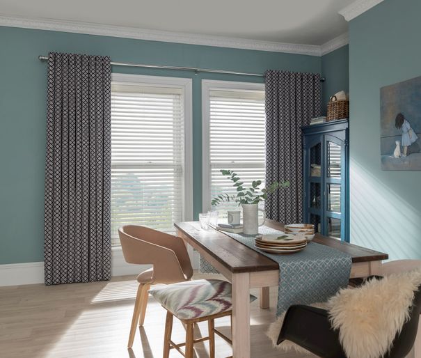Dining room with single window dressed in Faux-wood blinds and navy blue curtains