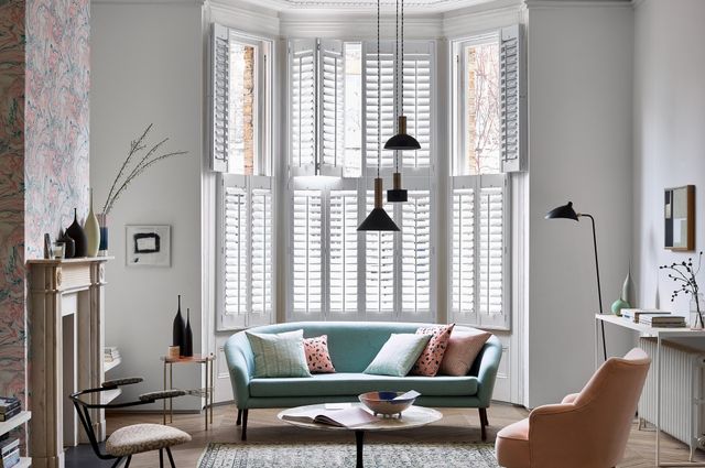 modern living room with blue sofa and full height white shutters in a bay window 