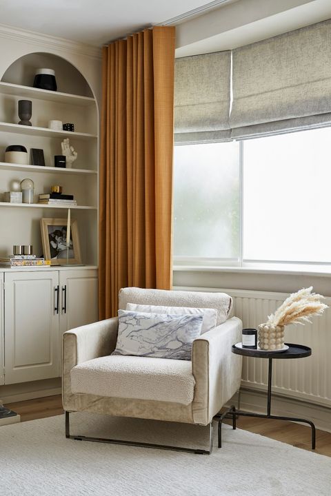 Orange full length curtains fitted to a rectangular shaped window along wth white roller blinds in a living room decorated in white