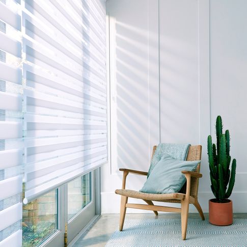 A wide window featuring a white Day & Night roller blinds and a chair