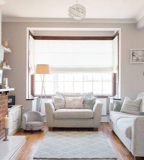 Cosy living room, with cream sofas, grey patterjed rug and a mixture of cusions featuring a white roman blind 