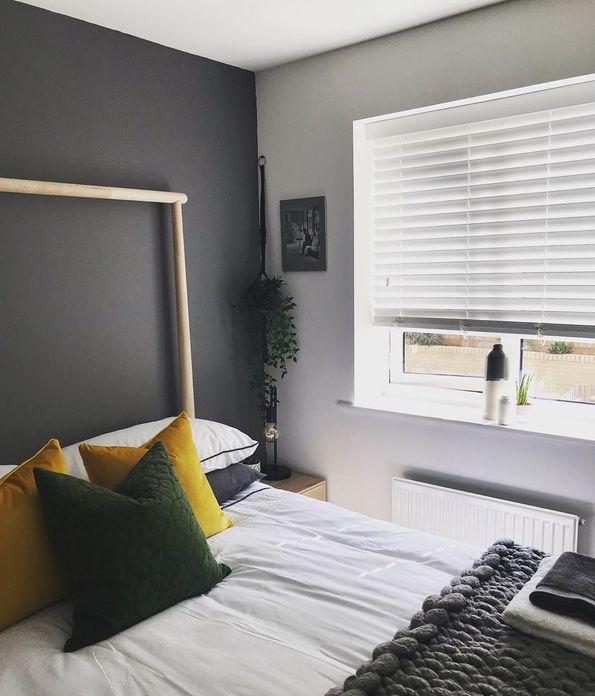 Grey tonal bedroom with yellow cushions and knitted blanket, white wooden ventian blinds 
