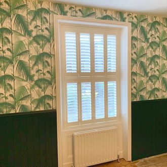 white shutters on windows and wall decorated with palm print wall paper