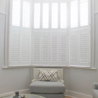 White tier on tier shutters in white living room with grey sofa and round glass table