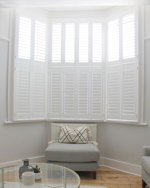 White tier on tier shutters in white living room with grey sofa and round glass table