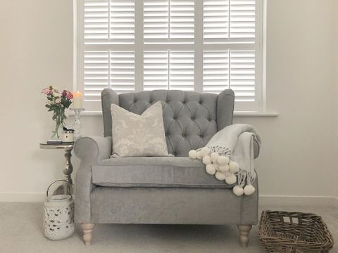 Shutter on window behind a grey snuggle chair in living room