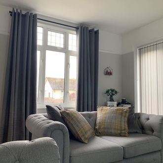 Windows in living room dressed with grey curtains behind grey sofa and side wall windows dresses with vertical blinds