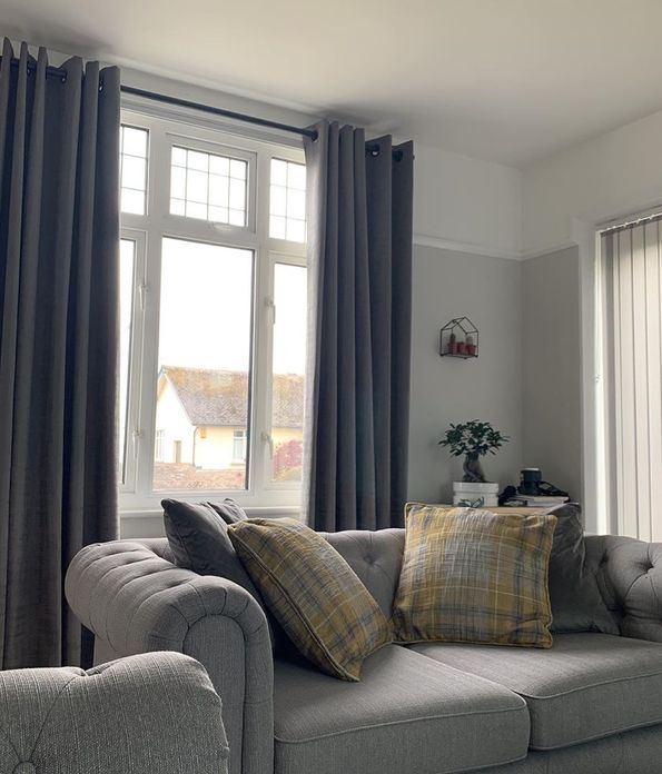 Windows in living room dressed with grey curtains behind grey sofa and side wall windows dresses with vertical blinds