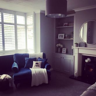 windows dressed with white shutters in a living room where blue sofa chair has been placed infront of windows, and natural light is coming in the room