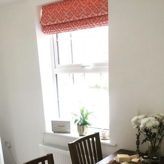 Coral and cream patterened roman blinds hanging on single hung window in dining room.