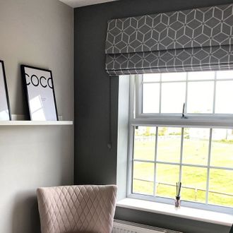 Window dressed with grey roman blind featuring geometric print in study