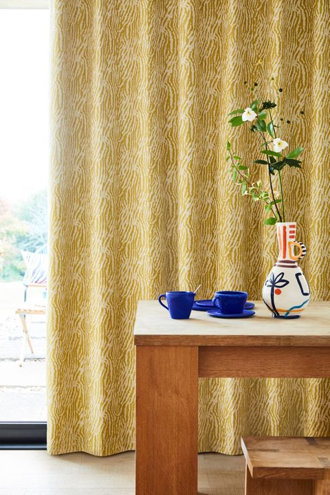 Citrine zebra print curtains hanging on the door. Blue cups and a flower vase is also placed on wooden coffee table in the corner of room.