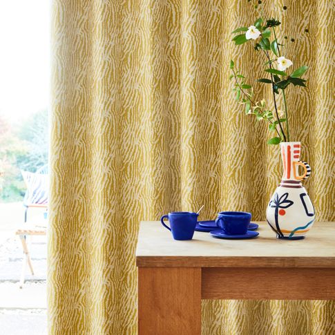 Citrine zebra print curtains hanging on the door. Blue cups and a flower vase is also placed on wooden coffee table in the corner of room.