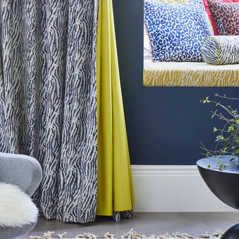 White and blue zebra print curtains with citrine lining hanging on wall. Matching Zebra print round small pillow, Blue and white Leopard print and Copper and black leopard print cushions have been placed in window seat.