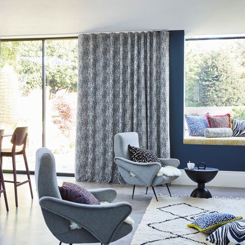 Blue and white zebra print curtains hanging on sliding doors of open plan kitchen and living area. Leopard, zebra and boho print cushions have been placed in window seat and resting chairs.