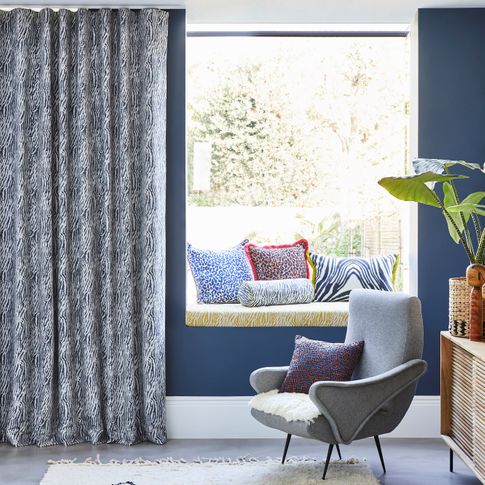 Blue and white zebra print curtains hanging on sliding doors of open plan kitchen and living area. Leopard, zebra and boho print cushions have been placed in window seat, resting chairs and on the rug