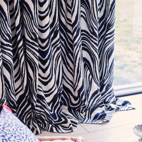 Close up of white curtains featuring some zebra print dressed on sliding door. A blue and white leopard print cushion have been placed on pink stool near the door.
