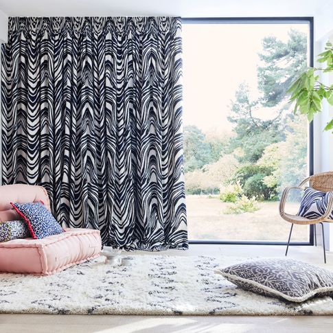 Blue and white zebra print curtains hanging on large window of garden room. Blue and white leopard print, black and white retro print, blue and white boho inspired print cushions have been placed on rug and chairs in the room.