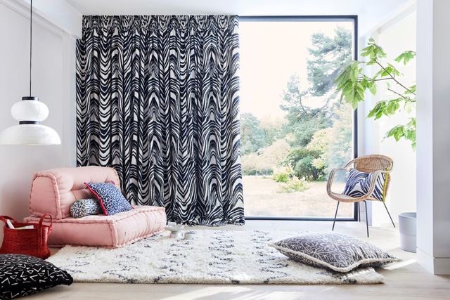 Blue and white zebra print curtains hanging on large window of garden room. Blue and white leopard print, black and white retro print, blue and white boho inspired print cushions have been placed on rug and chairs in the room.