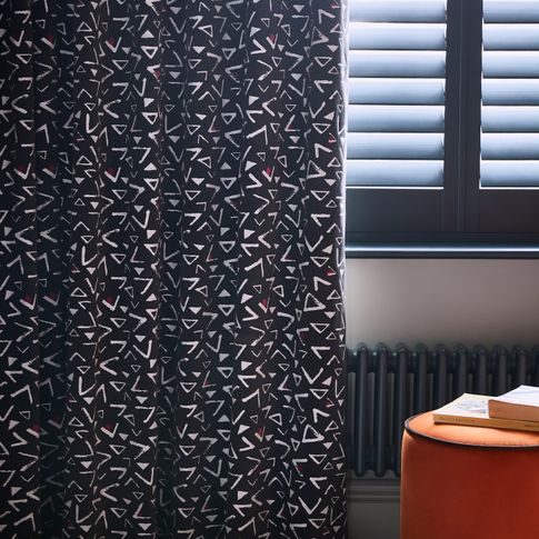Black and white retro print curtains over black cafe style shutters in a bedroom