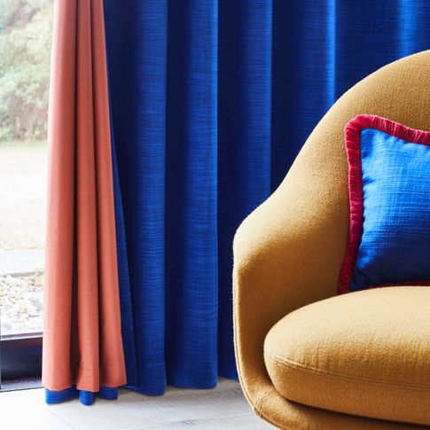 Dark blue curtain with rust color lining hanging on door, matching blue cushion with red fringe has been placed on mustard chair