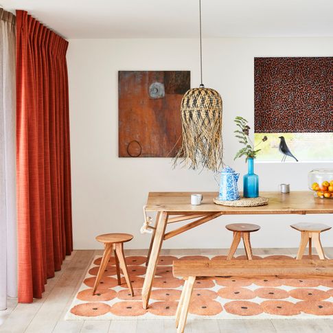 Orange curtians and white voile curtains are hanging on slding doors of dining room. Boho Inspired black orange printed roman blinds are dressed on the windows in the room.
