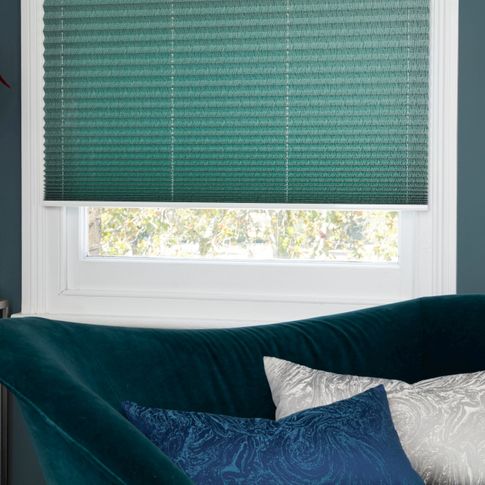 Green Pleated blinds from House Beautiful range dressed on windows in living room. Green velvet sofa has been placed by window.