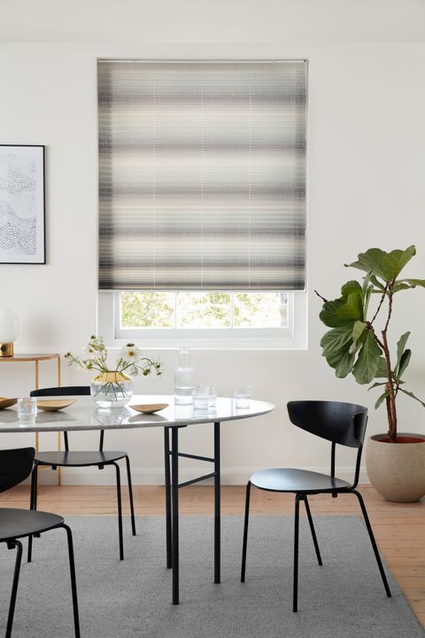 Mini stripe grey Pleated blinds from House Beautiful range hanging on single window in dining room. Grey dining table along with dark grey chairs is placed in room.