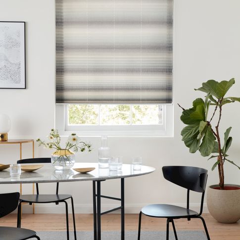 Mini stripe grey Pleated blinds from House Beautiful range hanging on single window in dining room. Grey dining table along with dark grey chairs is placed in room.