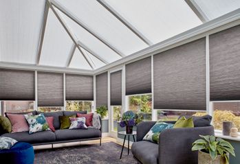 Charcoal Thermashade Pleated blinds at varying drop heights dressed on the windows in conservatory. Grey sofa with  cushions is placed in conservatory.