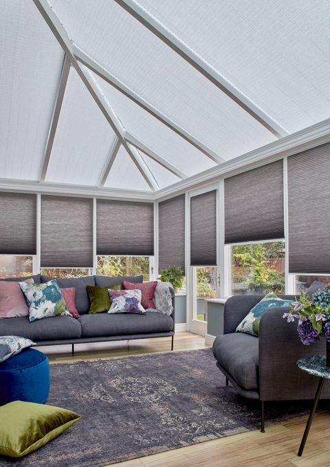 Charcoal Thermashade Pleated blinds at varying drop heights dressed on the windows in conservatory. Grey sofa with cushions and a large grey rug are also in situ.