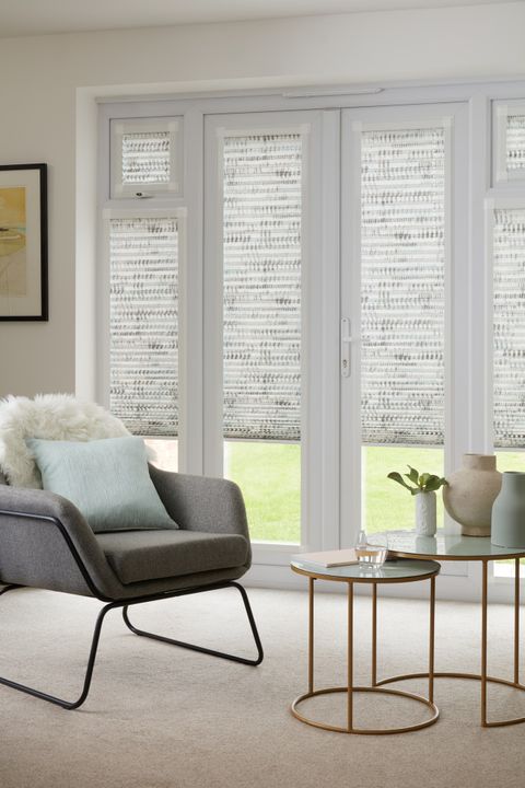 Duo natural Thermashade Perfect Fit Pleated blinds from House Beautiful range dressed on bifold doors of living room with smalll round table and grey chair with cushions.