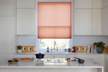 Peach Pleated blinds dressed on the windows of white painted kitchen with a few matching accessories on the units and island.